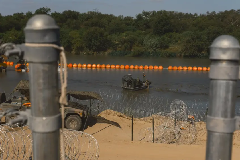 State law enforcement officers stand guard as workers construct a string of buoys being deployed to prevent migrants from swimming across the Rio Grande in Eagle Pass on July 14, 2023.