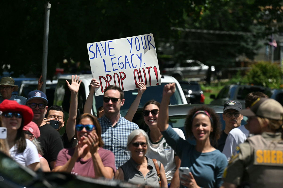 <i>Saul Loeb/AFP/Getty Images via CNN Newsource</i><br/>A person holds up a sign encouraging President Joe Biden to drop out of the 2024 presidential race as Biden's motorcade arrives at a campaign rally at Sherman Middle School in Madison