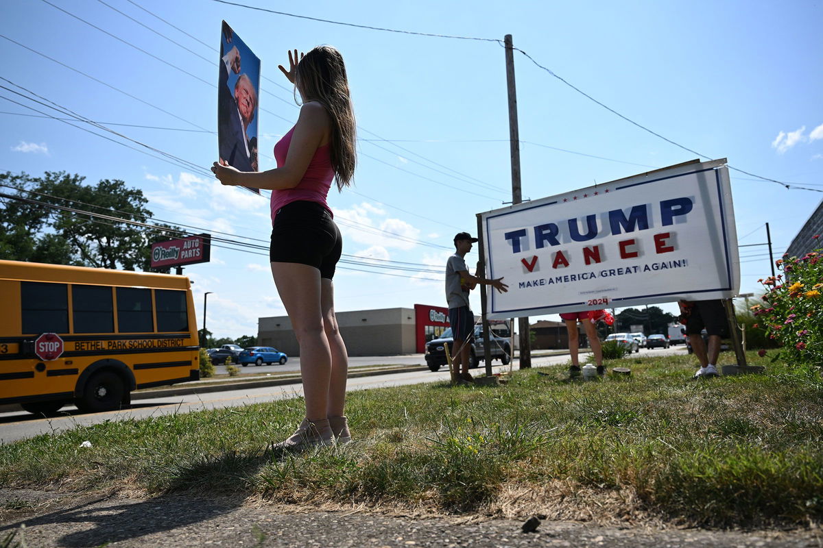 <i>Matt McClain/The Washington Post/Getty Images via CNN Newsource</i><br/>Julianna Grooms holds a photo of former President Donald Trump as neighbors help she and her mother secure a Trump yard sign that they used tape to add the name of Trump's running mate J.D. Vance outside their home on July 16