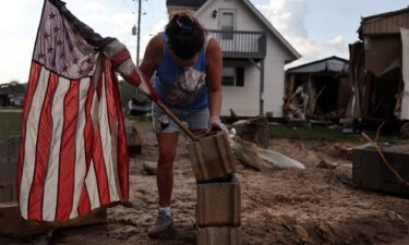 Roxanne Brooks mounts an American flag to a stack of cinderblocks outside her friend's destroyed mobile home (R) in the aftermath of Hurricane Helene flooding on October 6 in Swannanoa