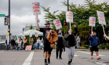 The image of a Boeing 737 jetliner is seen behind Boeing factory workers and supporters as they gather on a picket line during the third day of a strike near the entrance to a Boeing production facility in Renton