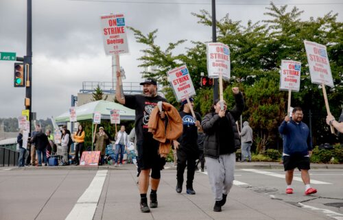 The image of a Boeing 737 jetliner is seen behind Boeing factory workers and supporters as they gather on a picket line during the third day of a strike near the entrance to a Boeing production facility in Renton